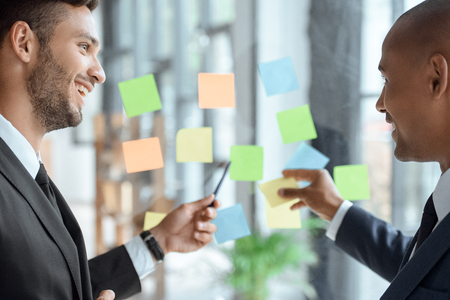 businessmen pointing at sticky notes while discussing workの写真素材