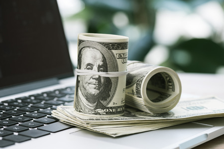 rolled dollar banknotes on opened laptopの写真素材