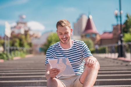 smiling tourist looking at map while sitting on stairs in cityの写真素材