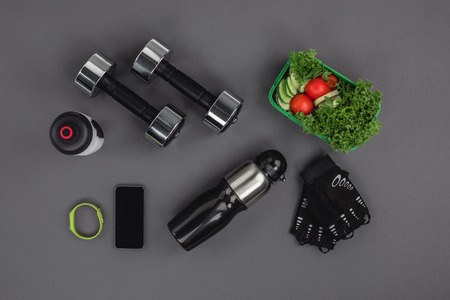 flat lay with smartphone with fitness tracker, dumbbells and vegetable salad isolated on greyの写真素材