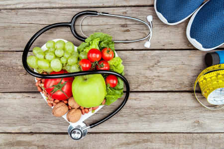 stethoscope, organic vegetables and fruits and measuring tape on wooden surface, healthy lifestyle conceptの写真素材