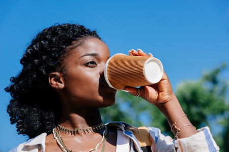 african american woman drinking coffee from disposable cupの写真素材
