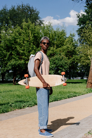 african american man holding longboard in parkの写真素材