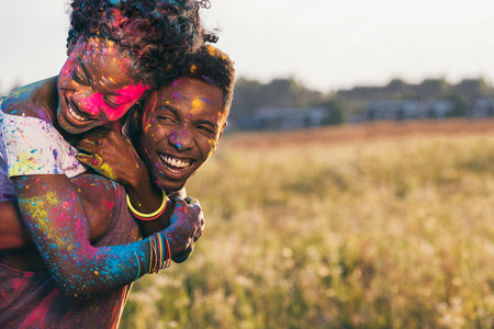 happy african american couple piggybacking at holi festivalの写真素材
