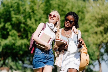 young multiethnic students smiling and talking while walking in parkの写真素材