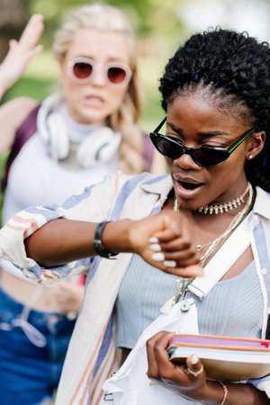 african american woman in sunglasses holding books and checking wristwatchの写真素材