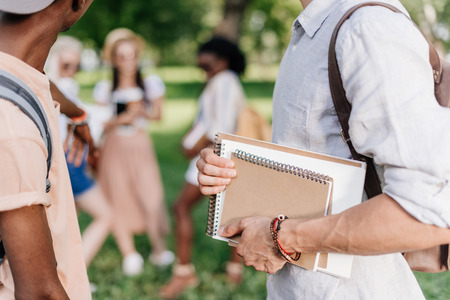 young students holding notebooks while standing in parkの写真素材