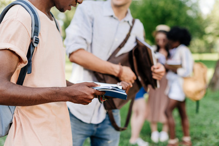 young students holding textbooks while standing in parkの写真素材