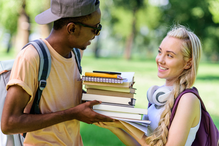 happy young multiethnic couple holding books together while standing in parkの写真素材