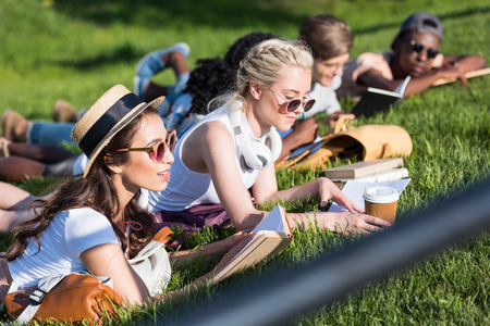 multiethnic girls reading books while lying on grass and studying in parkの写真素材