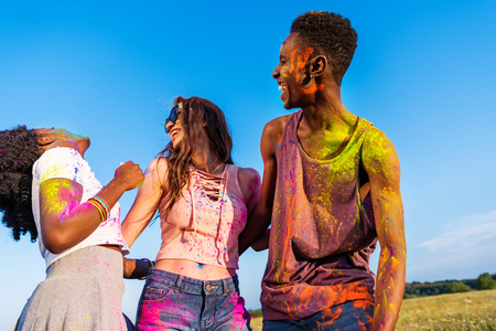 young multiethnic friends with colorful paint on clothes having fun together at holi festivalの写真素材