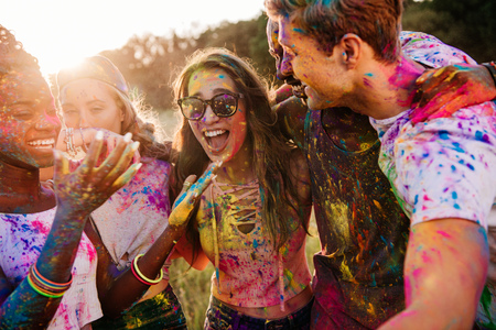 young multiethnic friends with colorful paint on clothes and bodies having fun together at holi festivalの写真素材