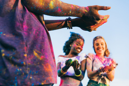 young man holding colorful powder while cheerful multiethnic girls standing behind at holi festivalの写真素材