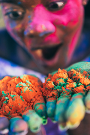 shocked african american girl blowing colorful powder from palms at holi festivalの写真素材