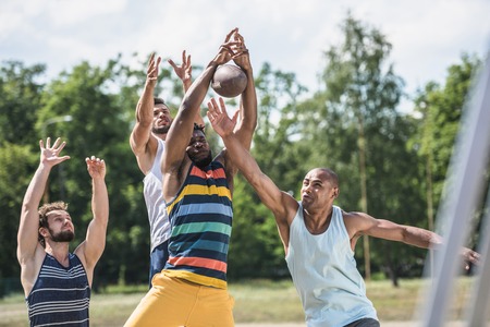 young multicultural men playing football on court