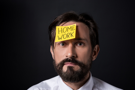 upset middle aged businessman with home work lettering on sticky note on forehead looking at cameraの写真素材