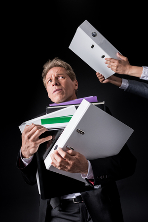scared overworked mature businessman holding pile of foldersの写真素材