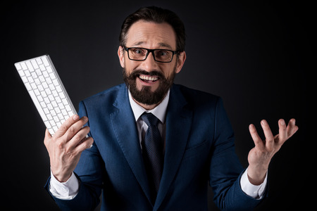 excited bearded businessman in eyeglasses holding keyboard and looking at camera