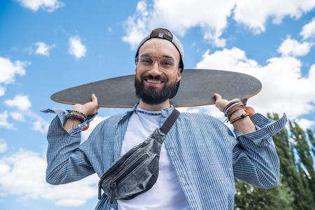 smiling man holding longboard on shoulders against blue skyの写真素材