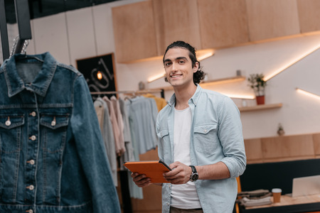 young man holding digital tablet and smiling at camera in boutique