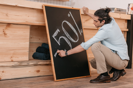 male seller drawing fifty percent discount sign on chalkboardの写真素材