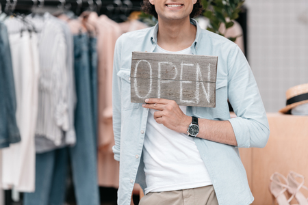 happy young shop owner holding open sign and smilingの写真素材