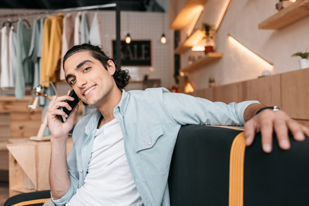 young shop owner talking on smartphone and smiling at cameraの写真素材