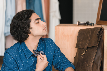 handsome young man choosing bow tie while looking away in boutiqueの写真素材