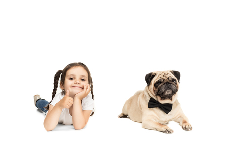 little adorable girl showing thumb up while lying with pug dog in bow tieの写真素材
