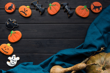 frame of homemade halloween cookies on black table with blue cloth and pumpkinsの写真素材