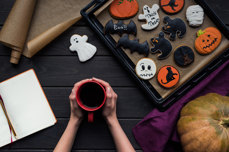 woman holding cup of coffee with tray of halloween cookies and blank notebookの写真素材