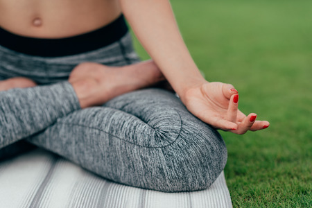 partial view of woman practicing lotus pose while meditating on green grassの写真素材
