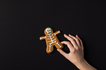 cropped shot of human hand with halloween cookie in shape of skeletonの写真素材