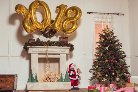 golden 2018 sign balloons above fireplace and christmas tree with gifts in empty roomの写真素材