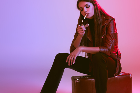 smoking girl sitting on suitcaseの写真素材