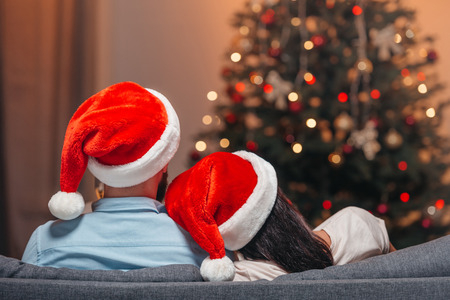 back view of couple in santa hats sitting together at homeの写真素材