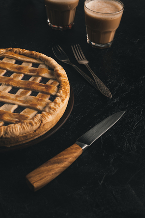 close up view of homemade apple pie, silverware and glasses of cacao isolated on black tableの写真素材