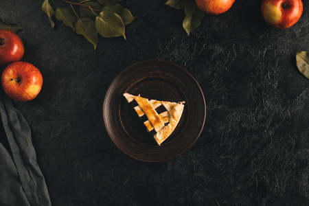 top view of piece of apple pie on plate, apples and leaves isolated on black surfaceの写真素材