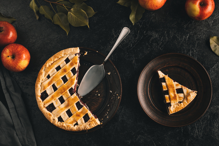 flat lay with arranged apple pie with cake server and fresh apples isolated on black surfaceの写真素材