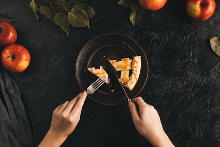 cropped shot of woman cutting piece of apple pie isolated on black tabletopの写真素材