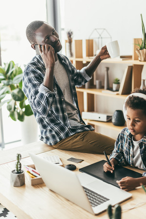 father talking by phone while son drawingの写真素材