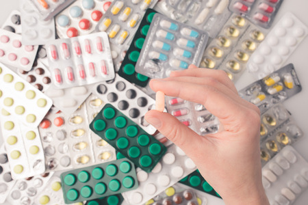 Cropped image of woman holding pill in hand on pile on blister packs 