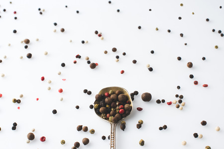 top view of spoon with spilled peppercorns isolated on white
