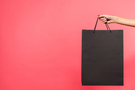 cropped shot of woman holding black shopping bag isolated on redの写真素材