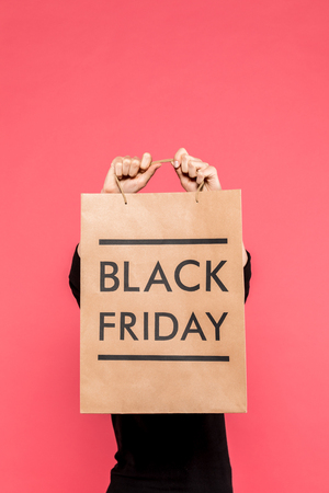 partial view of woman holding shopping bag with black friday lettering in hands isolated on pinkの写真素材