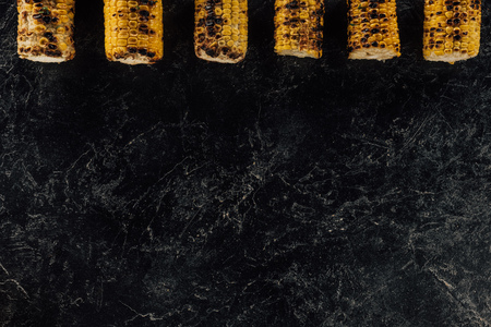 top view of row of grilled corn on concrete table
