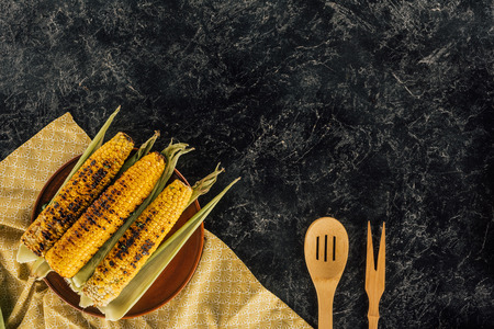 top view of grilled corncobs with wooden spatulas on dark concrete table の写真素材