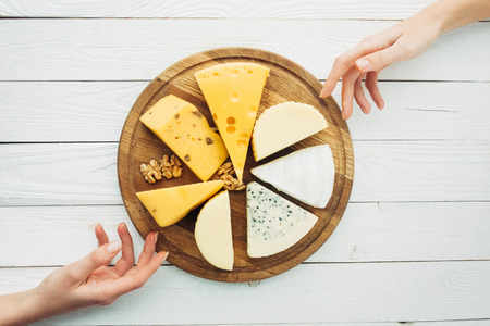 top view of female hands, arranged types of cheese and hazelnuts on wooden cutting boardの写真素材