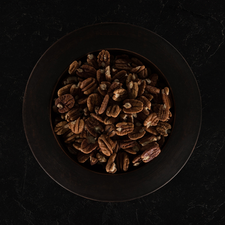 top view of delicious healthy pecan nuts in bowl on black  
