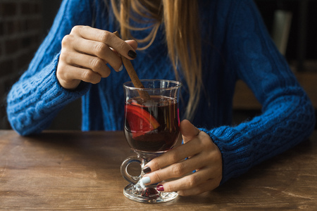 Cropped image of woman sitting at table and holding glass of mulled wine with cinnamon stick  の写真素材